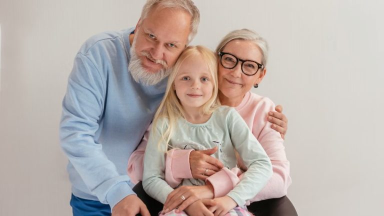 Loving grandparents embrace their smiling granddaughter in a cozy indoor setting.
